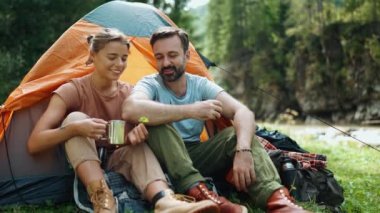 Olumlu turist çifti dağlarda çadırda otururken ağaç yaprağına bakıp konuşuyor.