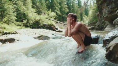 Gülümseyen turist kızıl saçlı adam dağlarda akan bir nehirde yüzünü yıkıyor.