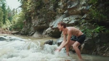 Dağlarda akan nehirde su sıçratan komik turist kızıl saçlı adam.