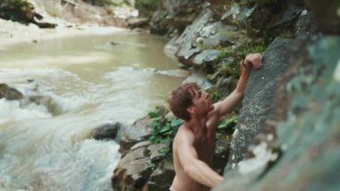 Güçlü turist kızıl saçlı adam dağlardaki nehirde bir kayaya tırmanıyor.