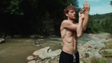 Dalgın kızıl saçlı adam dağlarda nehir kenarında spor egzersizleri yapıyor.