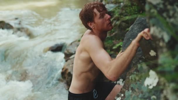 深刻な観光客の赤い髪の男は山の中で川に岩を登る — ストック動画