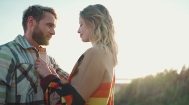 Güzel sarışın kadın erkek arkadaşının gömleğini düzeltiyor ve açık deniz kenarında sarılıyor.