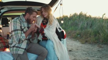 Battaniyeyle kaplanmış ve dışarıda arabanın bagajında konuşan mutlu sarışın çift.