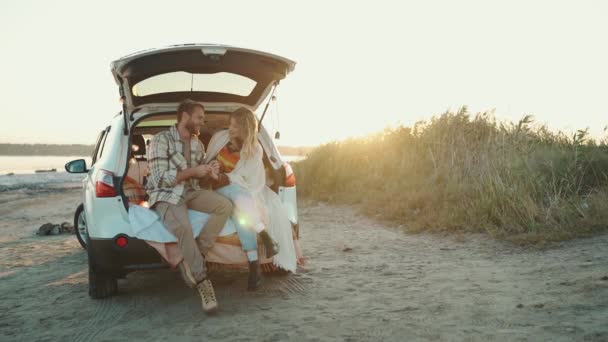 Pozytywna Blondynka Młoda Para Pokryta Kocem Rozmawiająca Bagażniku Samochodu Zewnątrz — Wideo stockowe