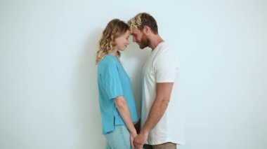 Güzel sarışın genç çift el ele tutuşup beyaz stüdyodaki kameraya bakıyor.