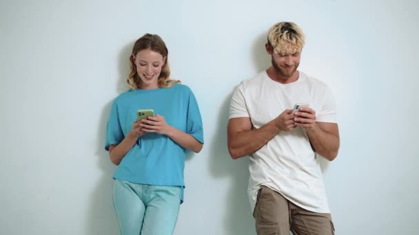 快乐的金发年轻夫妇在白色的工作室里用电话打字 — 图库视频影像
