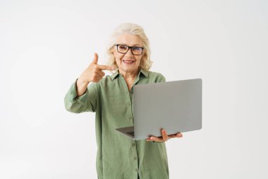 Gözlüklü, laptopunu işaret eden gri yaşlı kadın beyaz arka planda izole edilmiş.