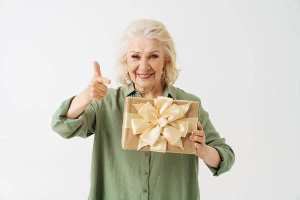 灰色老年妇女指指点点 在白色背景的相机前展示礼品盒 — 图库照片