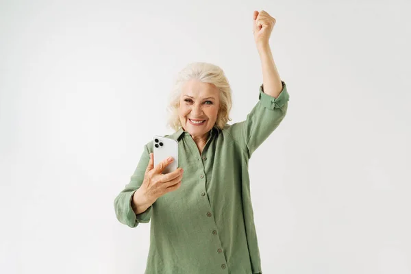 灰色老年妇女在与白人背景隔离的手机上玩网络游戏时摆姿势 — 图库照片