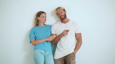 Gülen sarışın genç çift konuşuyor ve beyaz stüdyonun yan tarafını işaret ediyor.