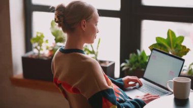 Laptopta çalışan ve kafede kahve içen pozitif sarışın kadın.