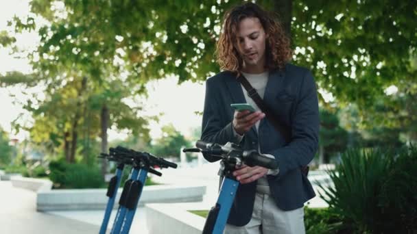 Concentrated Curly Haired Man Wearing Jacket Renting Scooter Outdoors — Stock Video