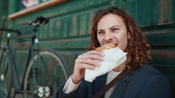 Feliz Homem Encaracolado Vestindo Casaco Comendo Croissant Café Livre — Vídeo de Stock