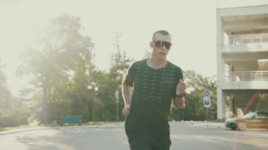 Gözlüklü konsantre sporcu yolda koşuyor.