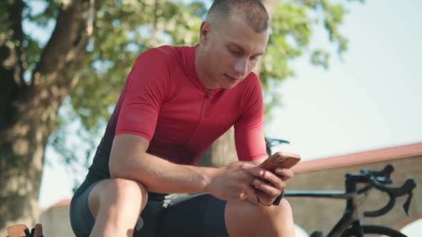 Esportista Concentrado Digitando Celular Banco Perto Bicicleta Livre — Vídeo de Stock