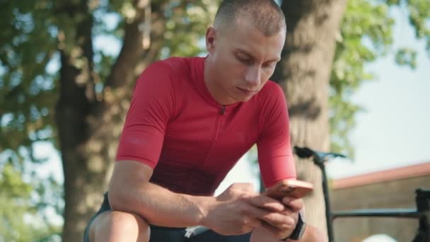 Desportista Sério Digitando Celular Banco Perto Bicicleta Livre — Vídeo de Stock