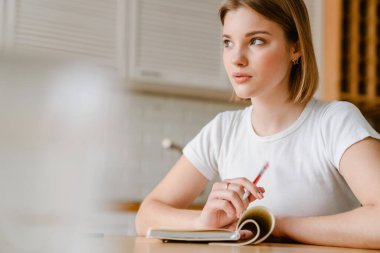 Gülümseyen genç kadın, evdeki mutfak masasında otururken günlüğünü yazıyor.