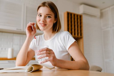 Gülümseyen genç kadın, evdeki mutfak masasında otururken günlüğünü yazıyor.