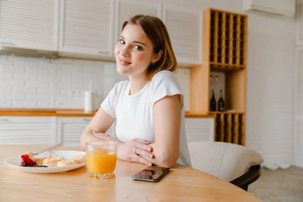 坐在厨房里吃着健康早餐的年轻女人笑着 — 图库照片