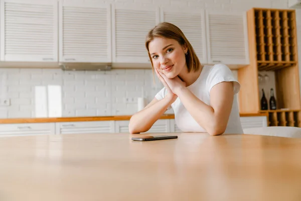 Usmívající Mladá Žena Sedí Kuchyňského Stolu Doma Mobilním Telefonem — Stock fotografie