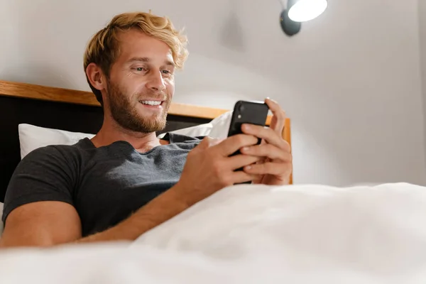 Rubia Barbudo Hombre Usando Teléfono Móvil Mientras Está Acostado Cama — Foto de Stock