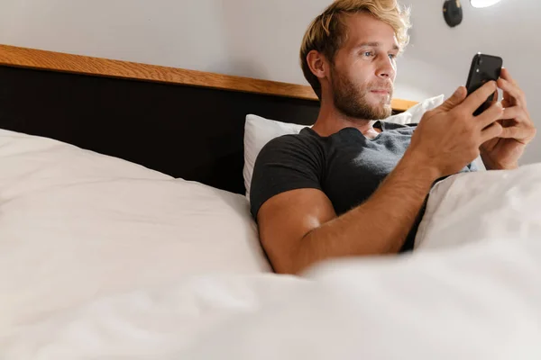 大胡子男人躺在床上用手机 — 图库照片