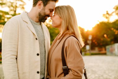 Sonbahar parkında yürürken gülümseyen ve sarılan beyaz romantik çift.