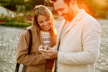 Sonbahar parkında yürürken gülümseyen ve cep telefonu kullanan beyaz bir çift.