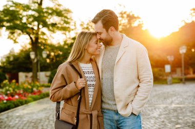 Sonbahar parkında yürürken gülümseyen ve sarılan beyaz romantik çift.