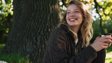 Parktaki piknikte çay içen genç bir kadın.