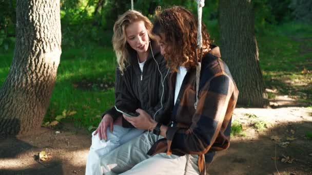 Gülümseyen Genç Çift Salıncakta Sallanıyor Parkta Telefona Bakıyor — Stok video