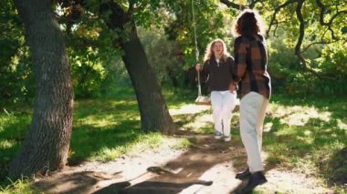 Gülümseyen kıvırcık saçlı adam parkta kız arkadaşını sallıyor.