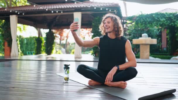 Kıvırcık Saçlı Neşeli Sporcu Dışarıda Yoga Minderinde Otururken Cep Telefonuyla — Stok video