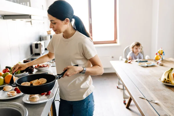 Sonriente Joven Madre Cocinando Desayuno Cocina Casa Pequeño Hijo Viendo — Foto de Stock