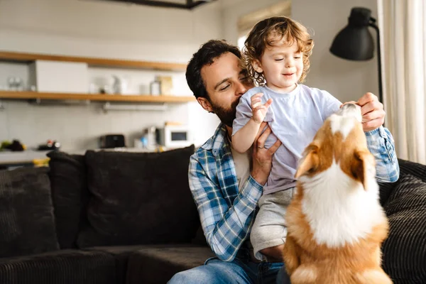 快乐的父亲和他的小儿子和他们的狗在家里的沙发上玩耍 — 图库照片