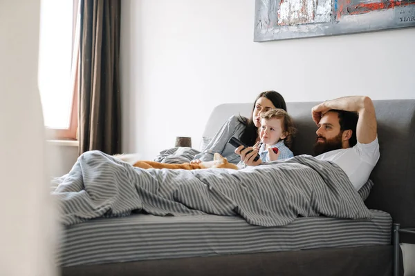 快乐的一家人早上一起在床上休息看电视 — 图库照片