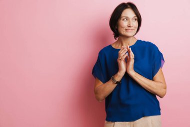 Pembe arka planda el ele tutuşurken gülümseyen olgun esmer kadın.