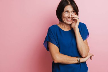 Olgun esmer kadın, pembe arka planda izole edilmiş yüzünü kapatırken gülüyor.