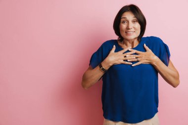 Olgun esmer kadın, pembe arka planda el ele tutuşurken gülümsüyor.