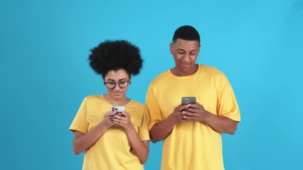 在蓝色工作室里穿着T恤衫在电话上打字的非洲夫妇 — 图库视频影像
