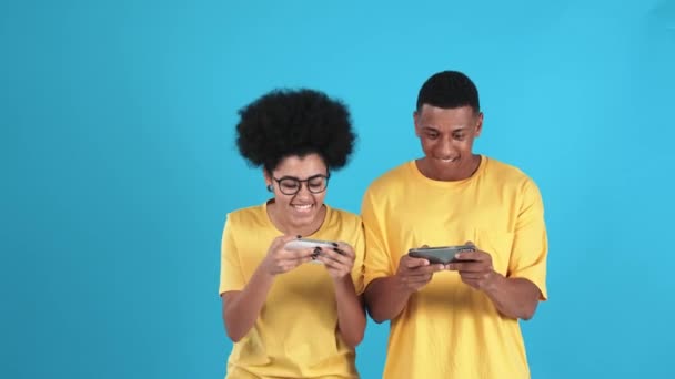 在蓝色工作室里 穿着T恤衫在手机上玩数字游戏的积极的非洲夫妻 — 图库视频影像