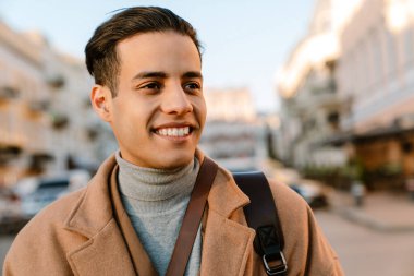 Şehir caddesinde yürürken gülümseyen ceketli genç adam.