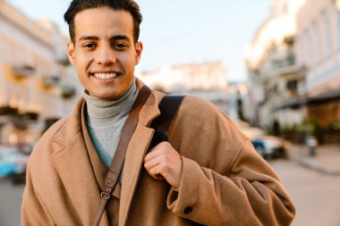 Şehir caddesinde yürürken gülümseyen ceketli genç adam.