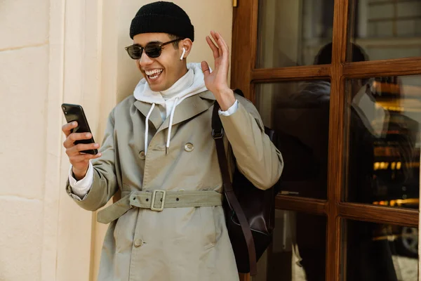 Młody Człowiek Uśmiechający Się Korzystający Telefonu Komórkowego Stojąc Przy Ścianie — Zdjęcie stockowe