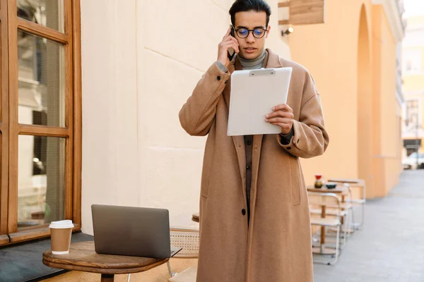 Młody Człowiek Płaszczu Rozmawiający Przez Telefon Komórkowy Podczas Pracy Kawiarni — Zdjęcie stockowe