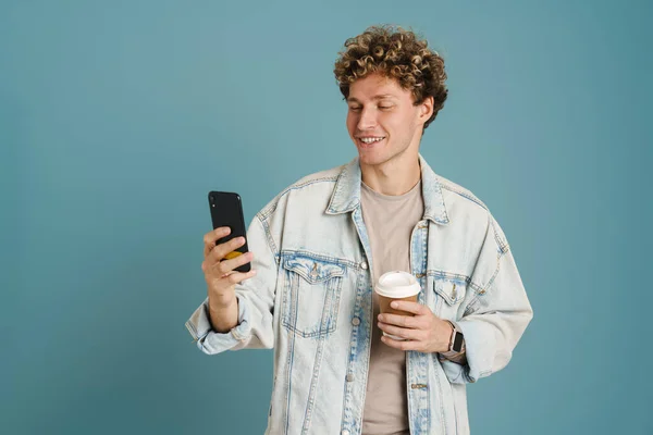 Ung Lockig Man Som Använder Mobiltelefon Medan Dricker Kaffe Isolerad — Stockfoto