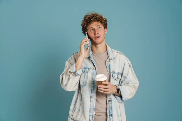 Młody Kręcony Mężczyzna Rozmawiający Przez Telefon Podczas Picia Kawy Niebieskim — Zdjęcie stockowe