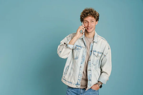 Junger Lockiger Mann Jeansjacke Spricht Auf Handy Isoliert Über Blauem — Stockfoto