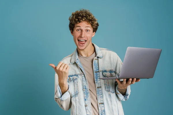 若いです興奮した男を使用してノートパソコンを指しながら指脇青の背景に隔離 — ストック写真